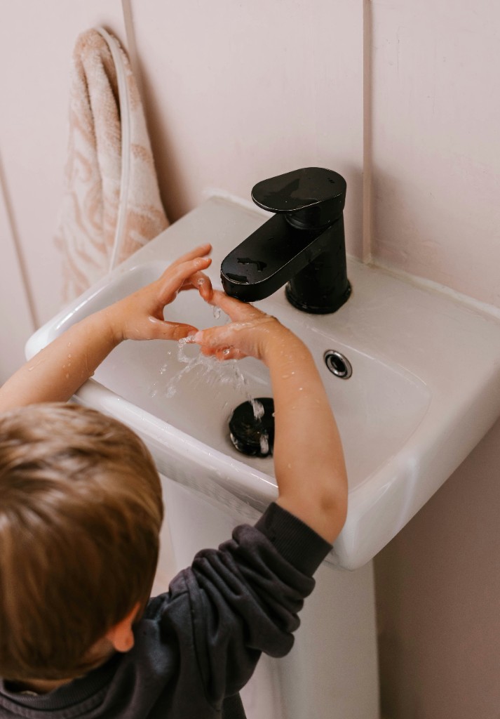 Child washing hands at a bathroom basin with a black mixer tap